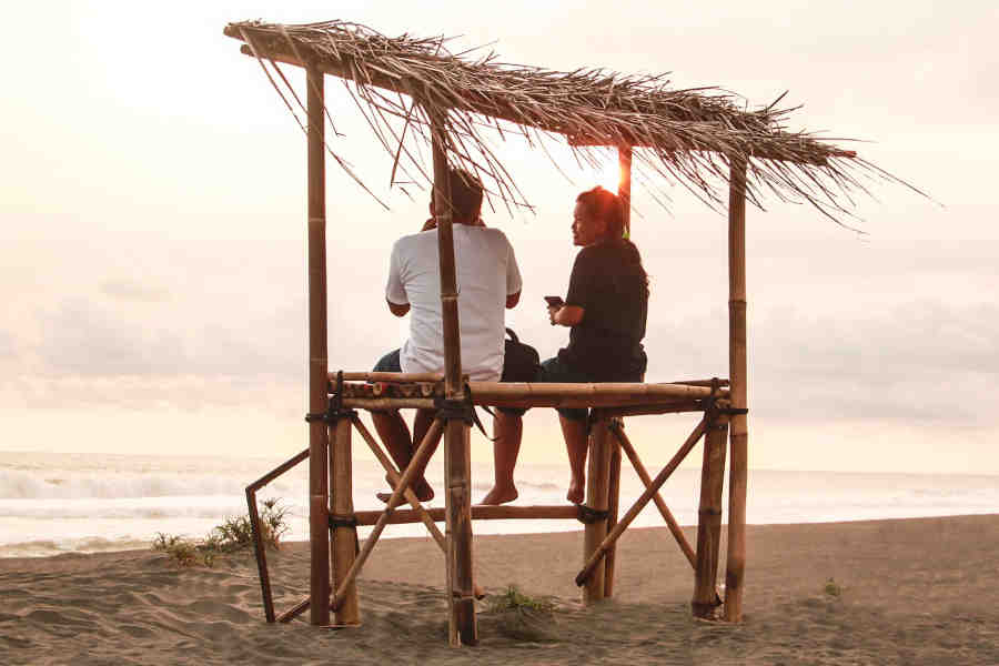 adult-couple-sitting-on-a-bamboo-furniture-with-roof-in-a-beach