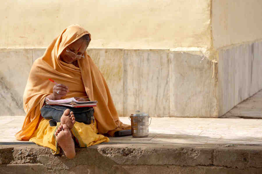 photo-of-an-old-and-a-traditional-indian-women-sitting-leg-streached-and-writing-in-a-paper-pad-and-a-pen